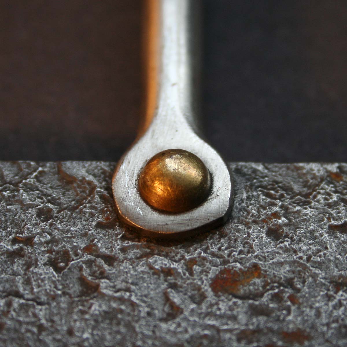 Forged and textured steel, stainless steel and a brass rivet